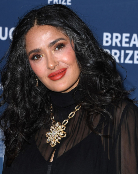 Salma Hayek posing in a sheer black top and gold necklace